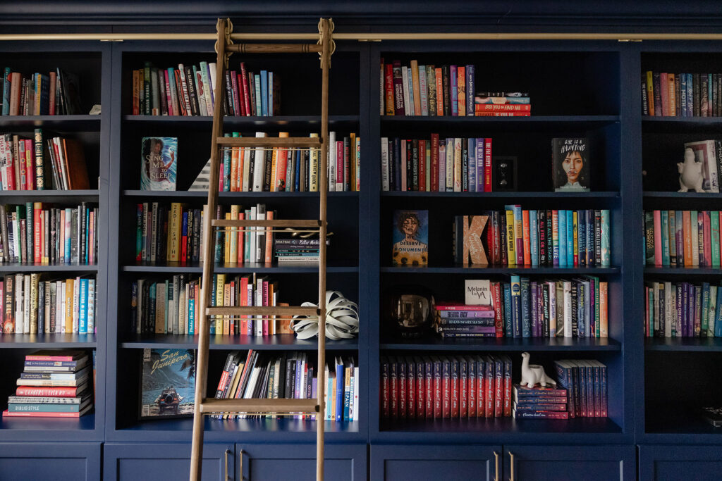 A cozy library room with navy blue bookshelves filled with colorful books and a wooden ladder — perfect inspiration for book lovers and home library design.

